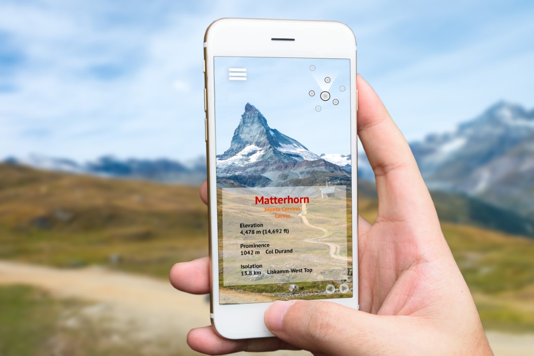Augmented reality marketing and travel 4.0 concept. Hand holding smart phone use AR application to check relevant information about the spaces around customer. Matterhorn mountain background