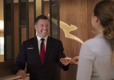 Passenger handing over boarding pass to a Qantas staff member at the reception of the Qantas business lounge in London